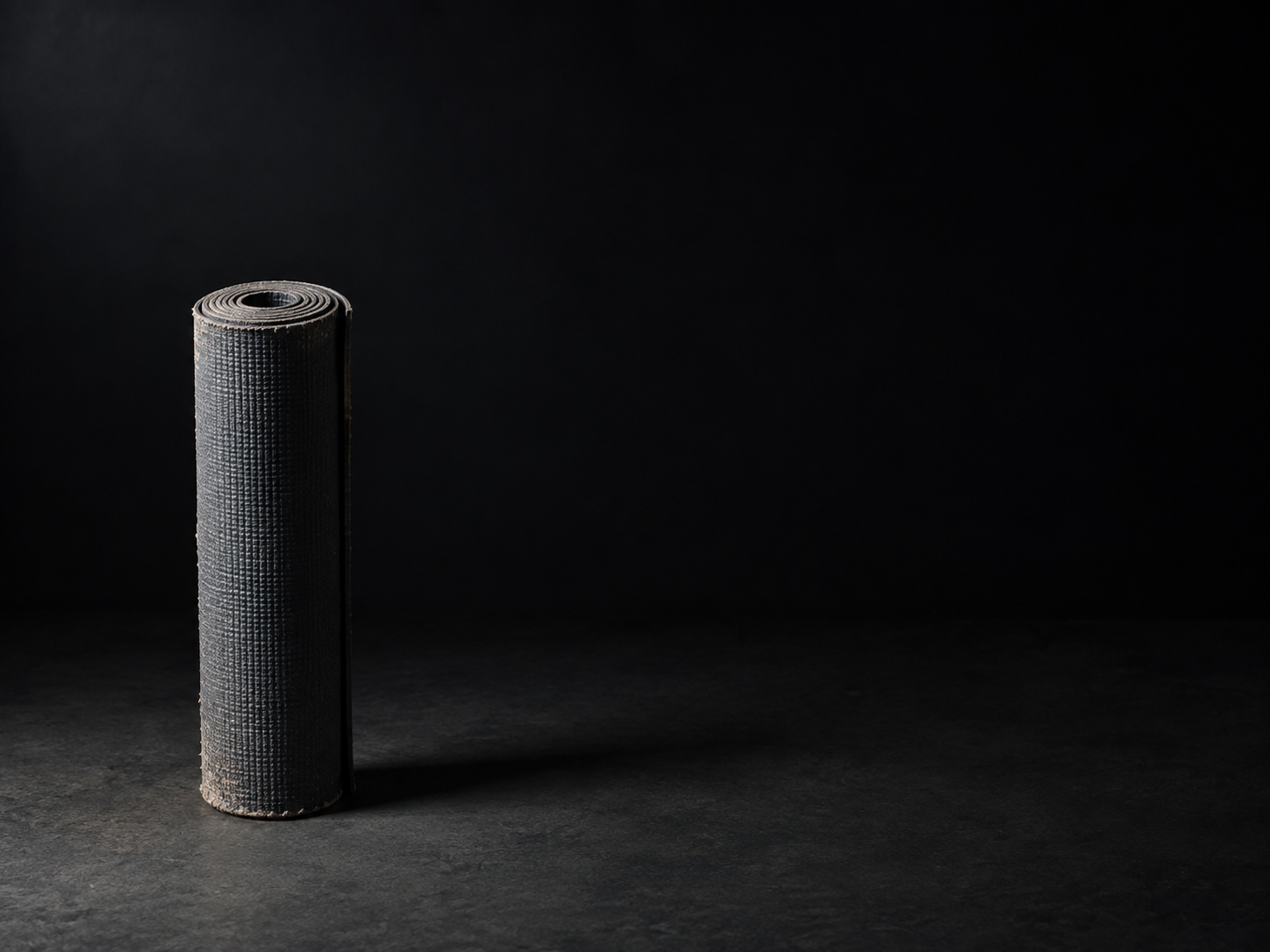 A worn rolled yoga mat lit from the left against a dark background
